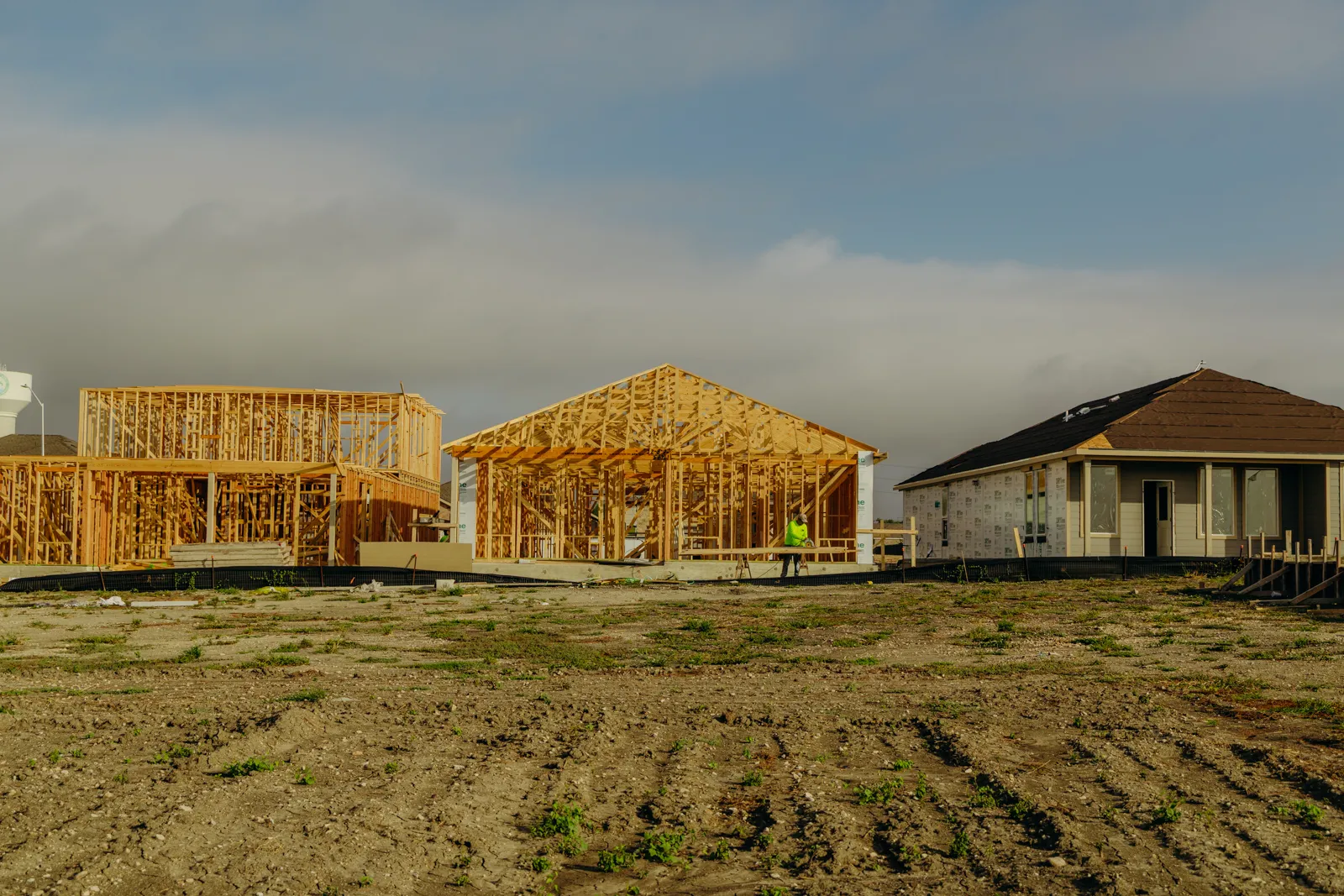 Wood framing going up on two houses beside a sheathed home