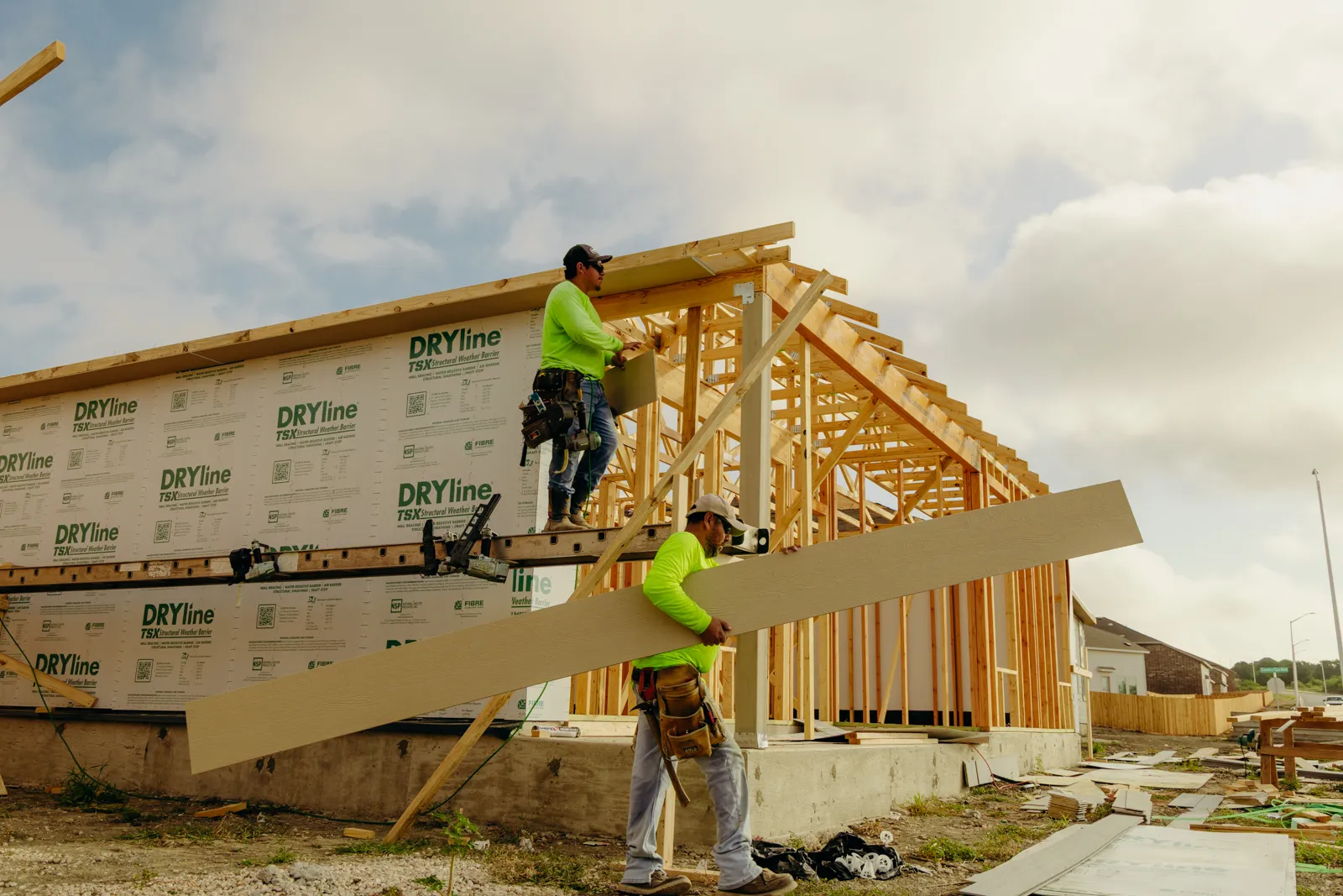Two carpenters framing a house, one carrying a board